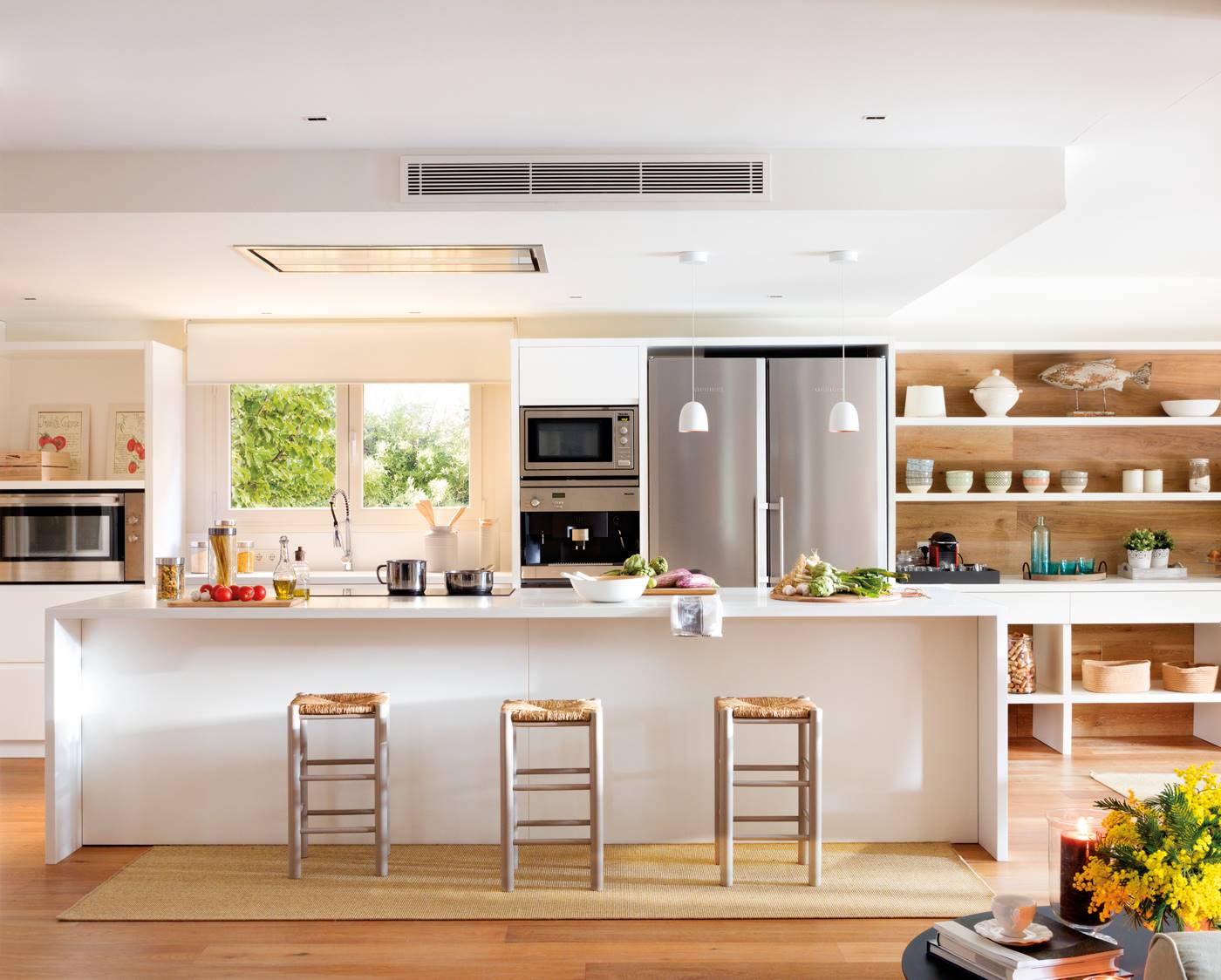 Cocina abierta y rectangular con isla alargada en blanco y suelos de madera. 