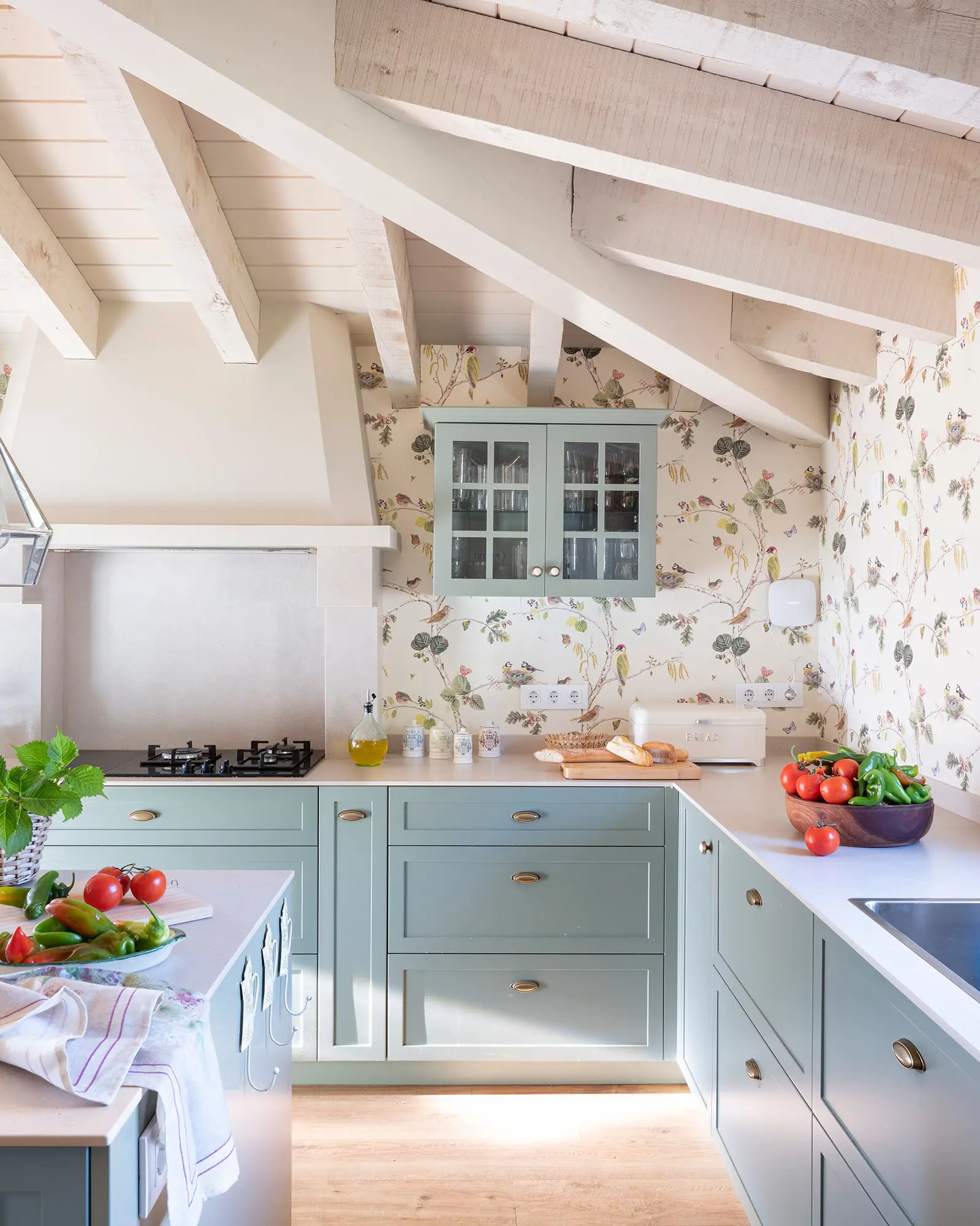 Cocina de casa de campo con muebles en azul y papel pintado de flores y aves.